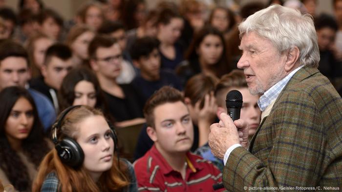 Hardy Krüger steht mit einem Mikrofon vor Jugendlichen 