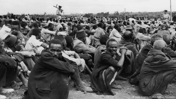 Hunderte Männer sitzen in der Hocke auf dem Boden, im Hintergrund ein Kolonialherr. (Getty Images/Hulton Archive/Keystone)