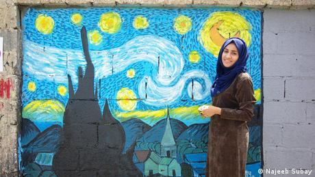 An woman standing in front of a mural in Sanaa (Najeeb Subay)
