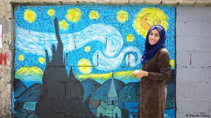 An woman standing in front of a mural in Sanaa (Najeeb Subay)