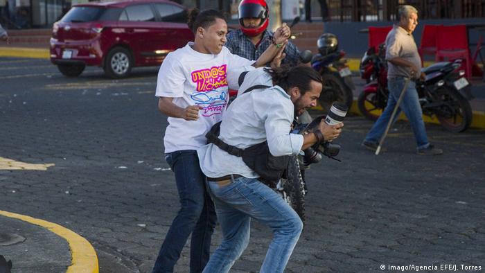 Ein junger Mann im T-Shirt der Ortega-Anhänger schlägt auf den Fotografen ein