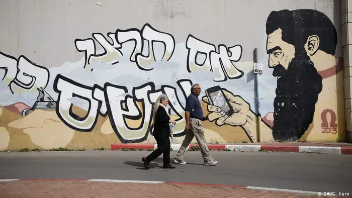 People walk past a graffiti showing Theodor Herzl, the father of modern political Zionism and referred to as the spiritual father of the Jewish State