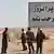 Syrian troops and pro-government gunmen standing next to a sign in Arabic which reads, "Deir el-Zour welcomes you," in the eastern city of Deir el-Zour, Syria.