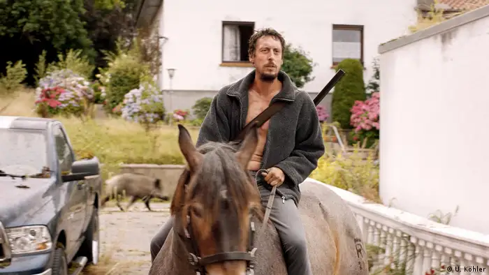 A man on a horse while a boar runs behind him from a film still 'In my Room' (U. Köhler)