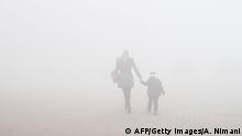 This photograph taken on January 30, 2018, shows a woman and child walking through heavy smog in the town of Obiliq on the outskirts of Pristina. Every winter morning workers wrap scarves around their faces and emerge from the pea soup fog that engulfs their town of Obiliq, stuck between two coal-fired power stations on the outskirts of Kosovo's capital. / AFP PHOTO / Armend NIMANI (Photo credit should read ARMEND NIMANI/AFP/Getty Images)