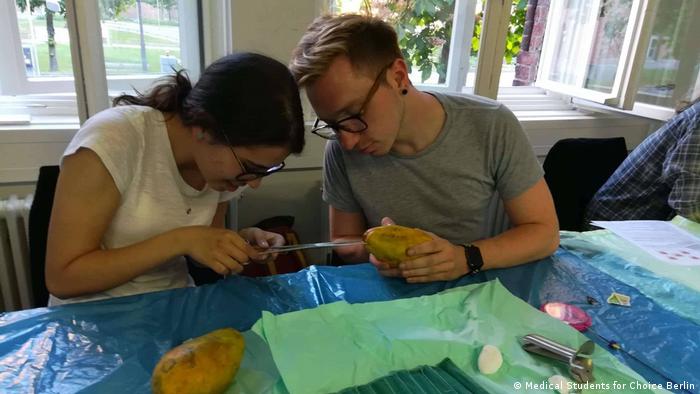 Two medical students practice conducting an abortion on a papaya