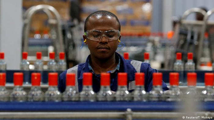 Schwarzer Arbeiter mit Schutzbrille zwischen Transportbändern für Flaschen in einer Fabrik für alkoholische Getränke in Nairobi
