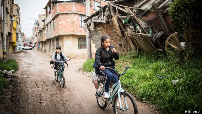 Ein Mädchen und ein Junge fahren auf Fahrrädern im Lisboa-Viertel in Kolumbiens Hauptstadt Bogota an einem verfallenen Gebäude vorbei