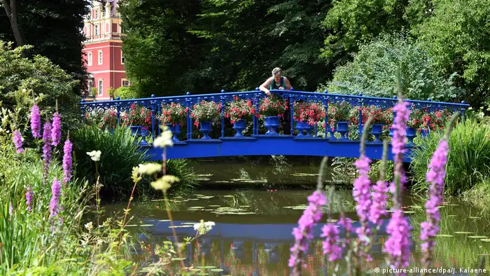 Brücke über einen Wasserlauf mit Blumen im Vordergrund, Schlossdetails im Hintergrund, Fürst Pückler-Park in Bad Muskau