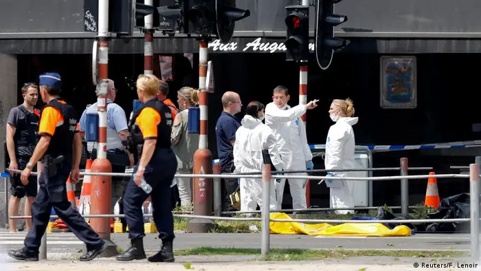 Especialistas forenses, vestidos de branco, conversam com um homem. 