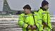 Uniformed, armed persons in bright yellow jackets. In the background a US transport aircraft Uniformed, armed persons in bright yellow jackets. In the background a US transport aircraft