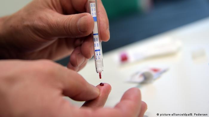 Ein junger Mann führt einen HIV-Heimtest durch. Man sieht eine Hand, eine Spritze und einen Tropfen Blut