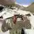 Soldado segurando fuzil no pescoço, diante de paisagem montanhosa nevada