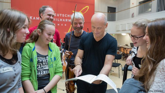 Paavo Järvi steht mit einer Partitur von Schülerinnen umringt. Paavo Järvi steht mit einer Partitur von Schülerinnen umringt.