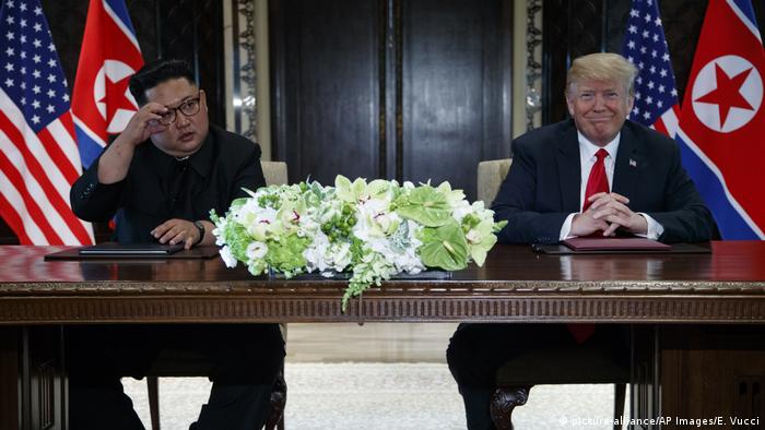 Kim Jong Un and Donald Trump sitting behind a desk.