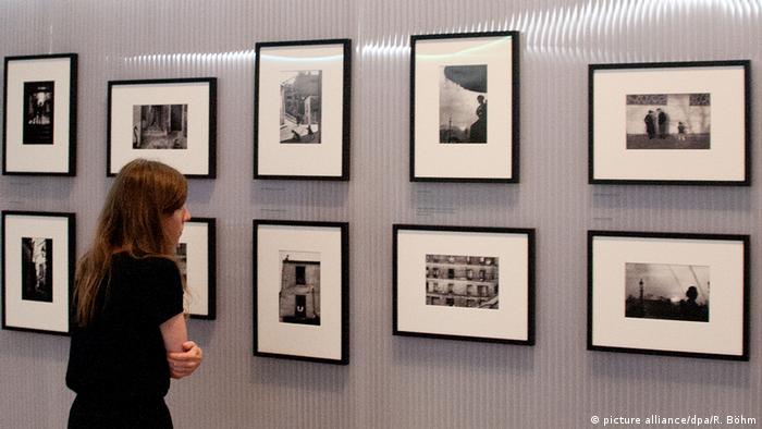 Eine Frau betrachtet an der Wand aufgehängte Schwarzweiß-Fotografien.