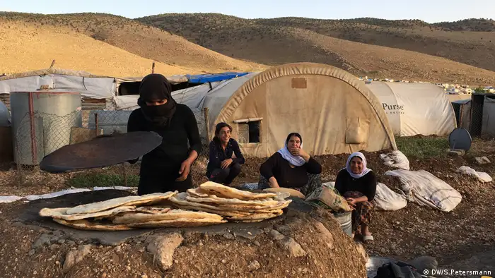 Irak, jesidische Frauen backen Brot im Lehmofen auf dem Mount Sinjar im Nordirak