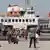 Emin Sarıoğlu waves a turkish flag as a people disembark on a pier from a ferry