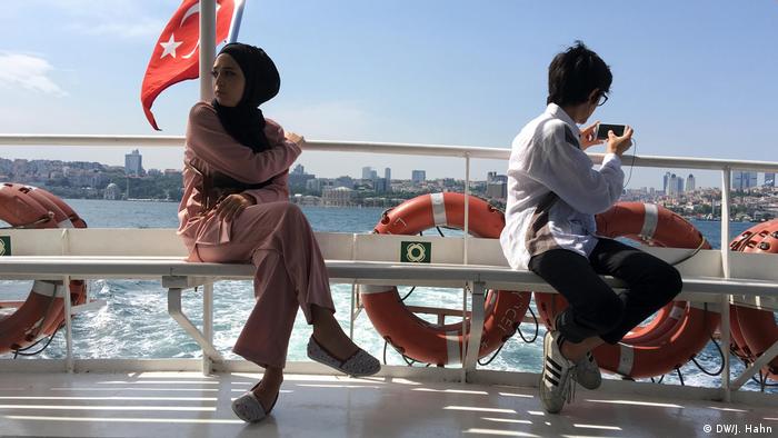 Two people sit on a ferry with the Istanbul skyline in the background