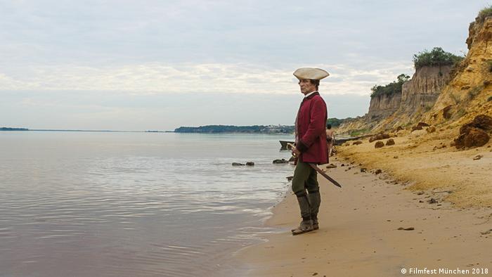 A man in a pirate outfit stands on the beach