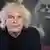 A portrait of Simon Rattle with an image of himself conducting behind him.