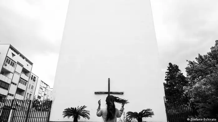 A woman standing in front of a cross on a white wall (Stefano Schirato)