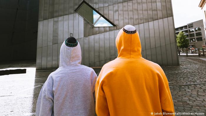 Two people wearing hoodies with kippot sewn on top stand outside the Berlin museum