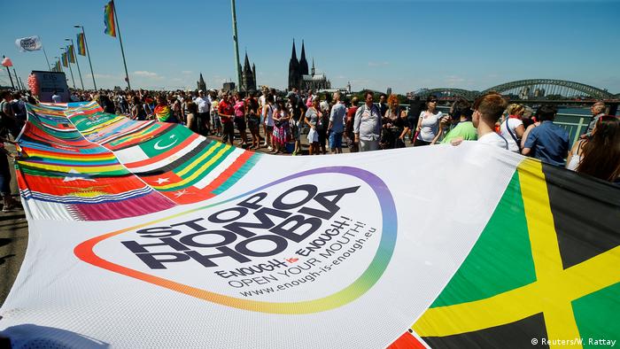Pride marchers carry a massive banner with the flags of the world and a 'stop homophobia' segment.