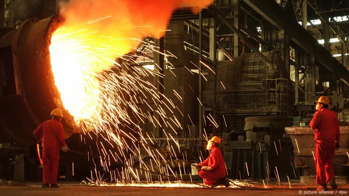 Tres trabajadores alrededor de un alto horno en una planta siderúrgica.