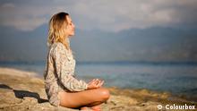 Woman sitting in lotus position on rock by the sea