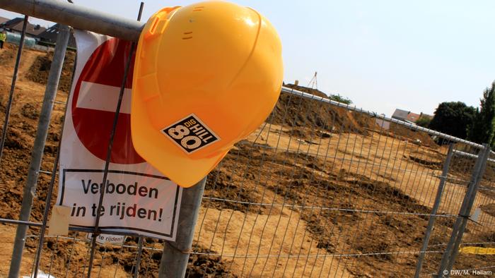Archaeological dig site at Wijtschate, Belgium, excavating remnants of a World War I trench network; photo taken 06.07.2018. A protective hard hat with the project's Dig Hill 80 logo hangs on the security fence cordoning off the site. (DW/M. Hallam)
