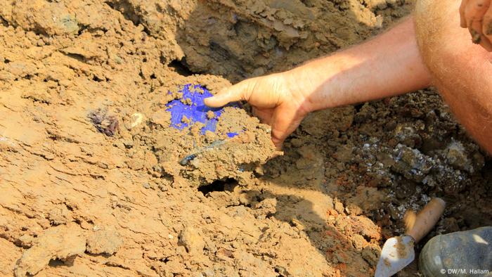 Archaeological dig site at Wijtschate, Belgium, excavating remnants of a World War I trench network; photo taken 06.07.2018. An archaeologist extracts a blue water bottle, believed to have belonged to a French soldier. Several bottles and other equipment like toothbrushes were discovered in this location. (DW/M. Hallam)