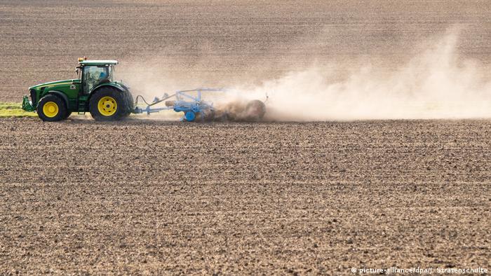 A farmer drives across a field dried out by the heat