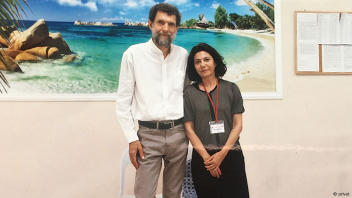 Osman Kavala visited by his wife, Ayse Bugra, in prison. A big picture of the Mediterranean is in the background.