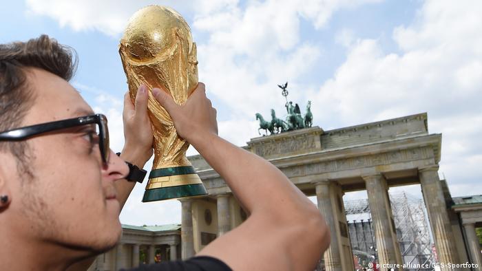 Mesut Özil holds the 2014 World Cup trophy in front of Berlin's Brandenburg Gate