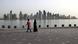 Two people walk in front of a wide view of the Doha skyline Two people walk in front of a wide view of the Doha skyline