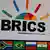 A woman walks past a large billboard with the acronym BRICS and a picture of former South African leader Nelson Mandela next to a colorful graphic of a rising sun
