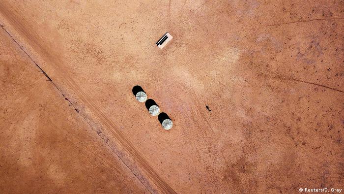 Farmer walks near a water trough and tanks on his drought-affected property (Reuters/D. Gray)
