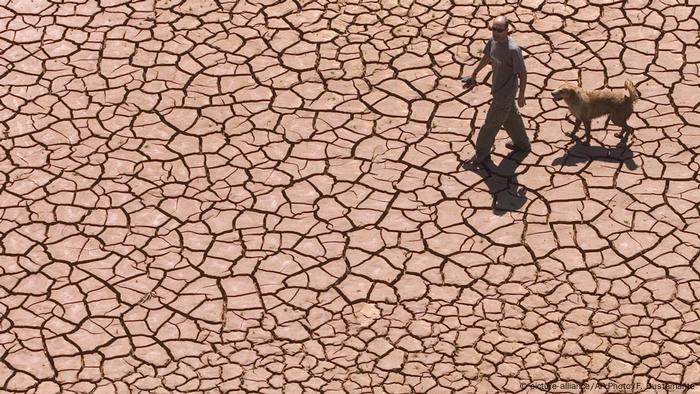 Man walking with dog on cracked, dried earth of Alcora Lake in Spain