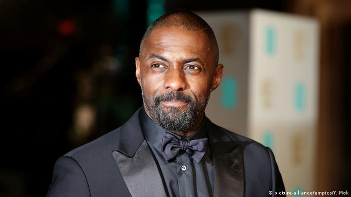 Bust shot of Idris Elba wearing a black-on-black tuxedo.