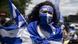 A person in a Nicaraguan flag marches wearing a headband that reads Nicaragua Libre A person in a Nicaraguan flag marches wearing a headband that reads Nicaragua Libre