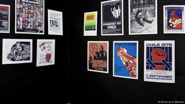 Exposición de afiches, sobre pared negra, con lecturas en alemán.
