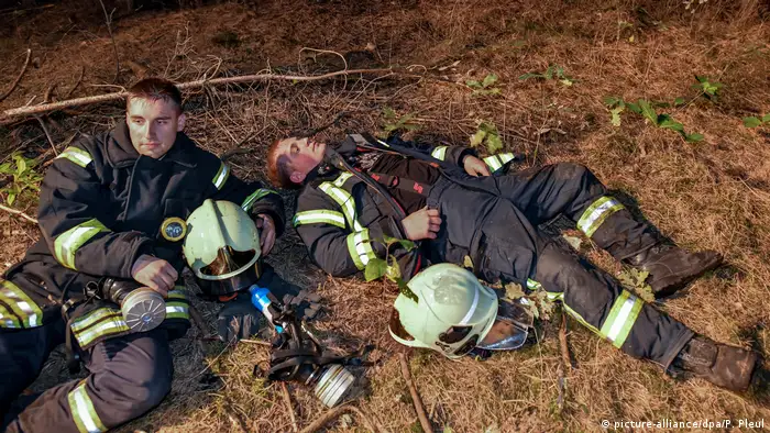 Feuerwehrmänner liegen auf dem Waldboden (Foto: picture-alliance)