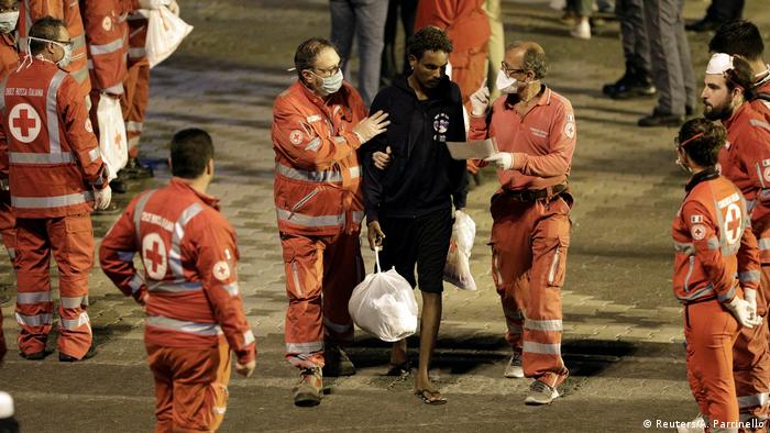 A migrant is led away by Red Cross workers