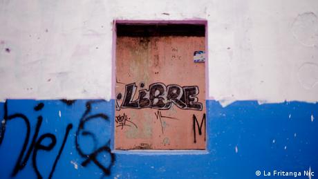 Exposición fotgráfica Miradas en Resistencia. Las calles que resisten, muro de una casa pintada con los colores de la bandera azul y blanco. En el centro una ventana con la palabra escrita libre (La Fritanga Nic).