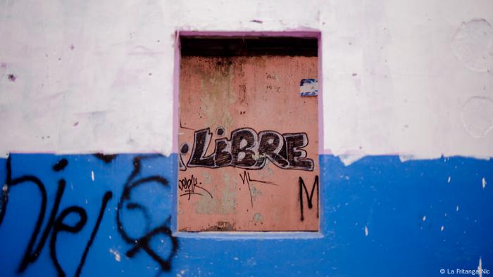 Exposición fotgráfica Miradas en Resistencia. Las calles que resisten, muro de una casa pintada con los colores de la bandera azul y blanco. En el centro una ventana con la palabra escrita libre (La Fritanga Nic).