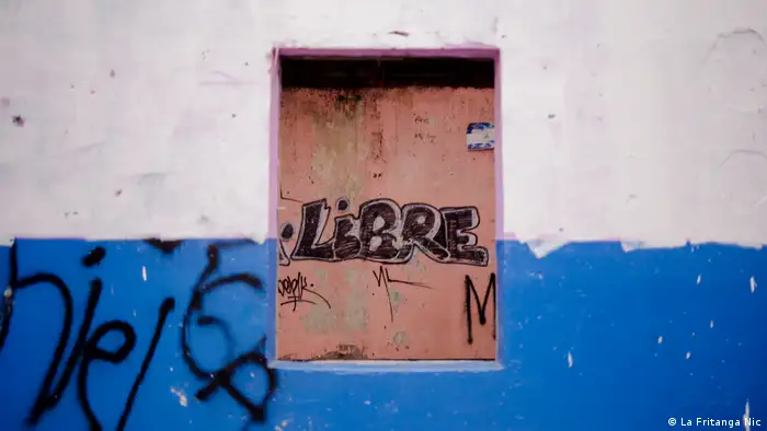 Exposición fotgráfica Miradas en Resistencia. Las calles que resisten, muro de una casa pintada con los colores de la bandera azul y blanco. En el centro una ventana con la palabra escrita libre (La Fritanga Nic).