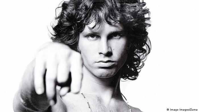 Jim Morrison, young man looks into camera, stretches out right arm 