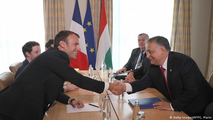 Macron and Orban shaking hands across a table