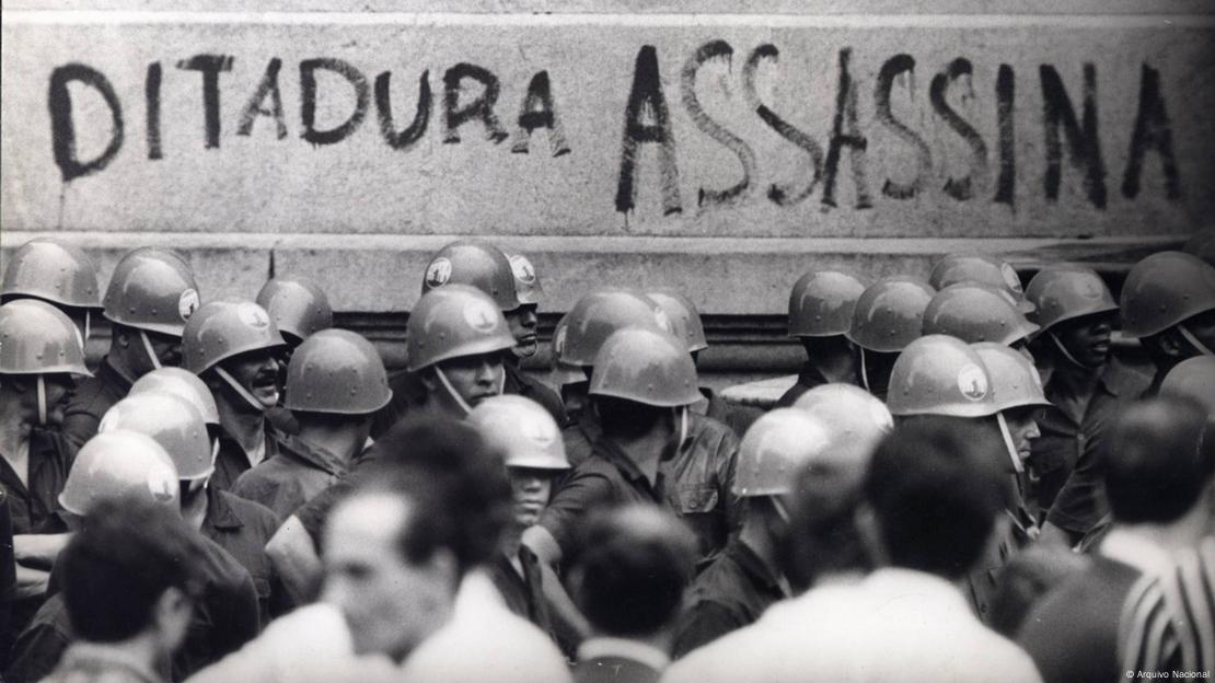 Soldados em frente a muro onde se lê Ditadura Assassina